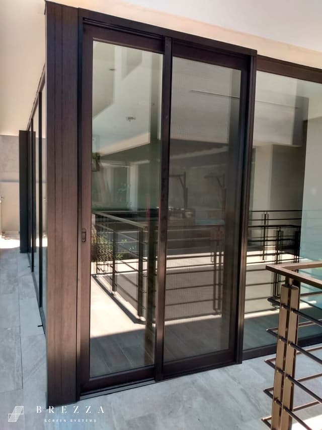 Vista frontal de un mosquitero Brezza marrón con el tipo Astuto instalado en ventanas correderas que están cerradas