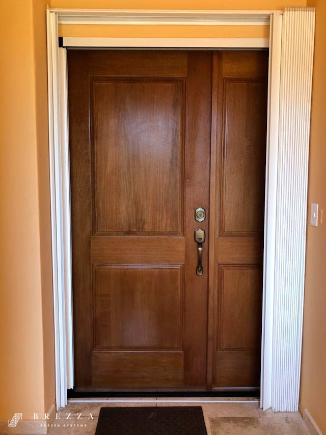 Vista frontal de un Brezza Mosquitero tipo Astuto blanco en una puerta delantera que está cerrada